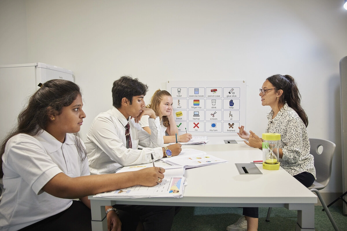 Group of three teenagers sat at a table, talking to a staff member