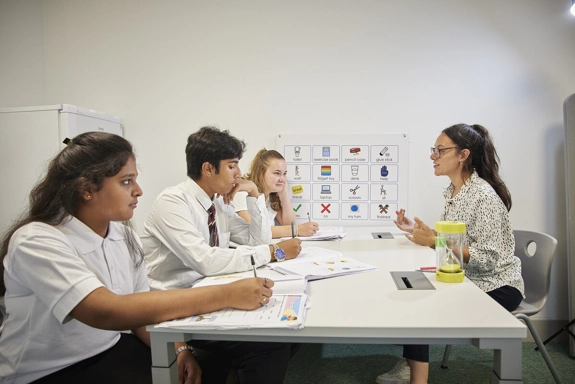 Group of three teenagers sat at a table, talking to a staff member
