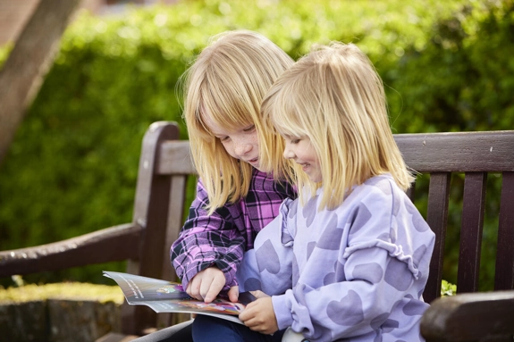 Two children reading a book on a bench outside