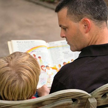 Dad reads a book to his son - photo taken from behind as if someone looking on