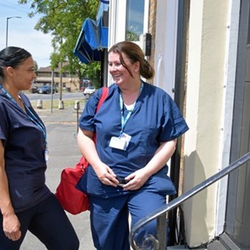 Two NHS workers in uniform stood talking to each other outside