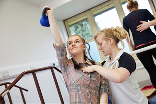 An MSK specialist assisting a patient with exericse using a weight and an inflatable ball