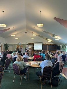 Event space with lots of attendees. One person presenting to the group.