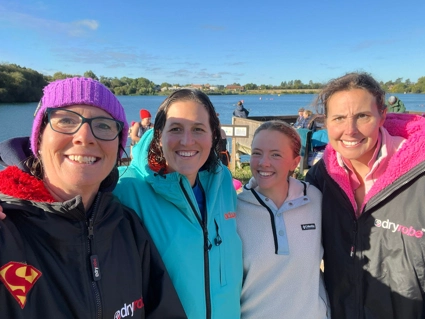 A selfie photo of four team members, smiling in front of lake