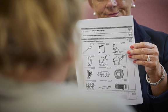 A closeup photo of a person holding up a test page of different pictures to a patient.