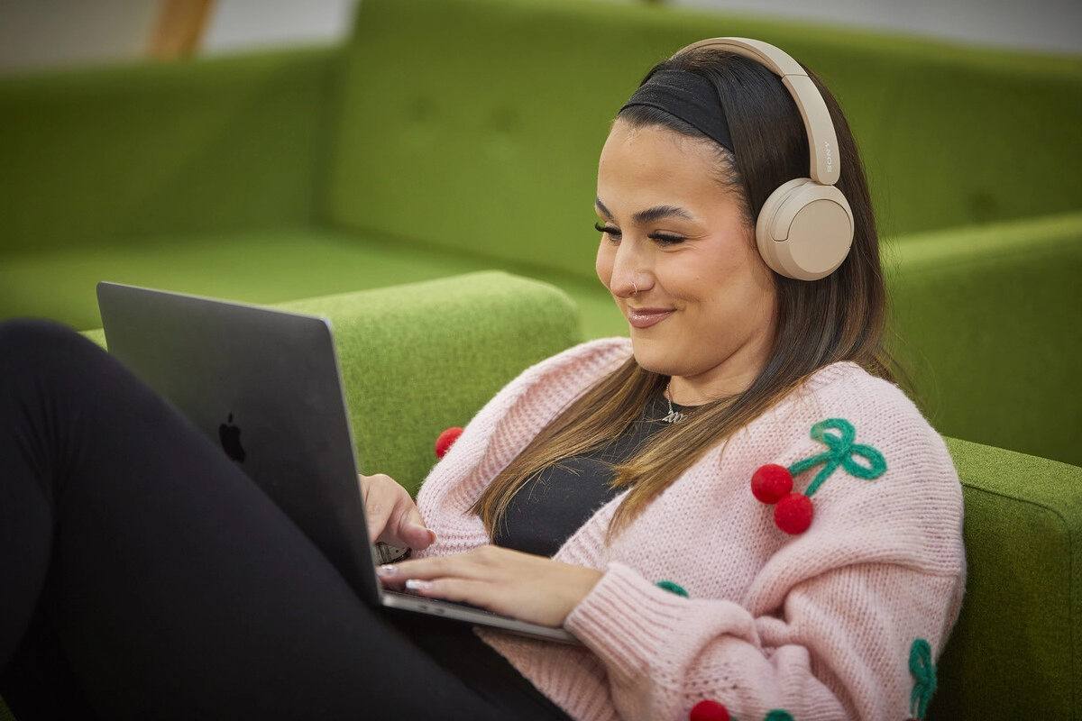 A person sat smiling using a laptop, and wearing headphones
