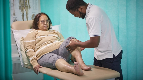 Physiotherapy patient in bed having knee bent by physio