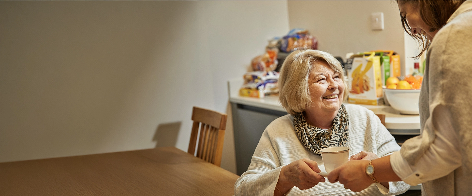 Carer passing tea to older woman