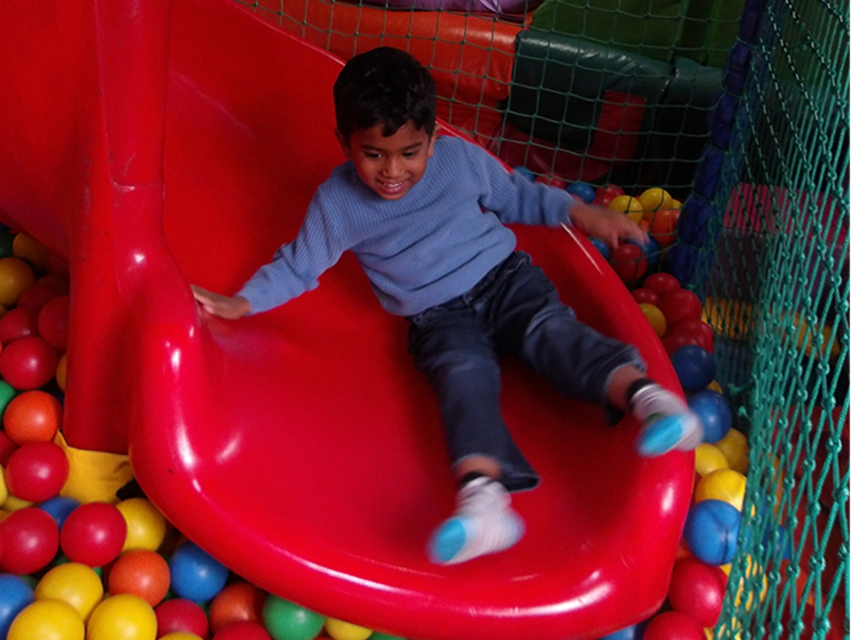 A child smiling on a slide, landing into a ball pit at soft play