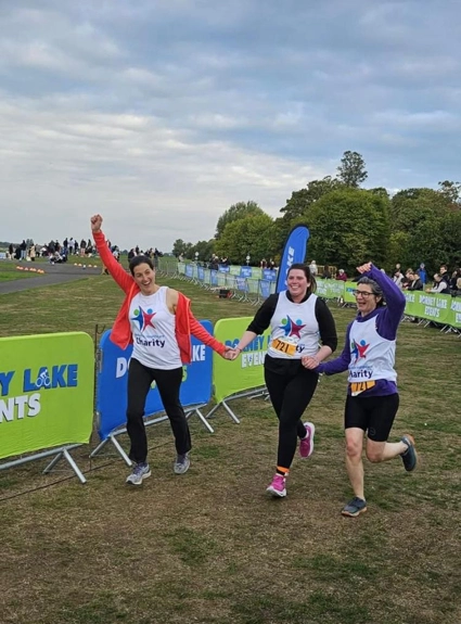 Three team members, running and holding hands, finishing the triathlon