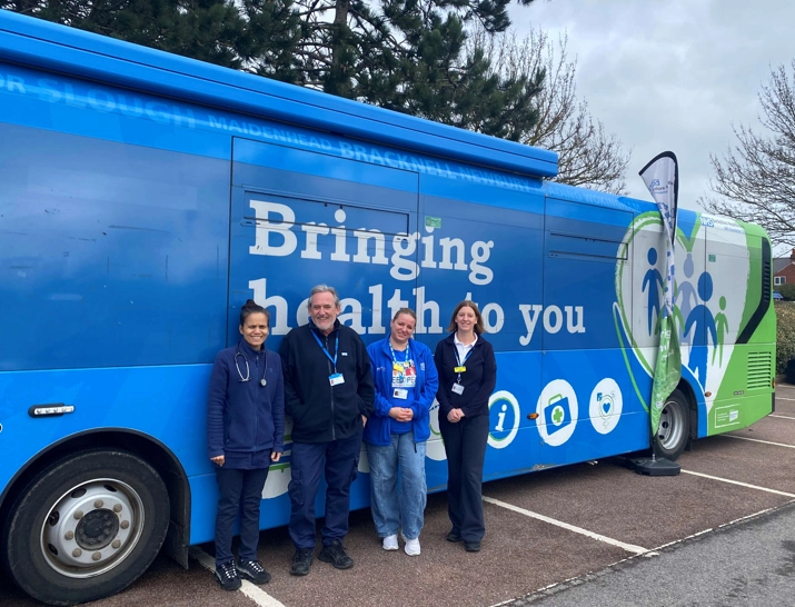 Four staff members smiling, stood outside against the Health Bus