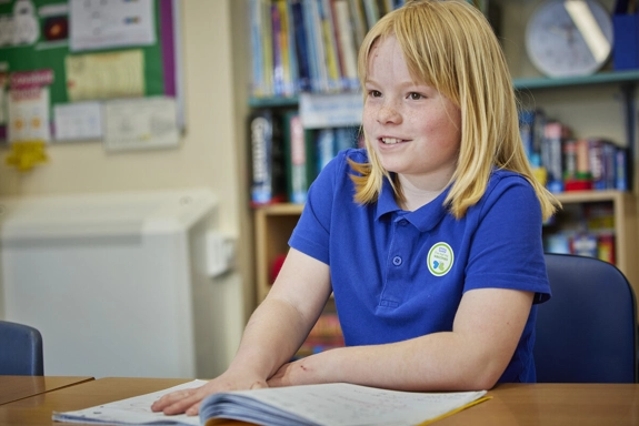 School child at desk in classroom with book open