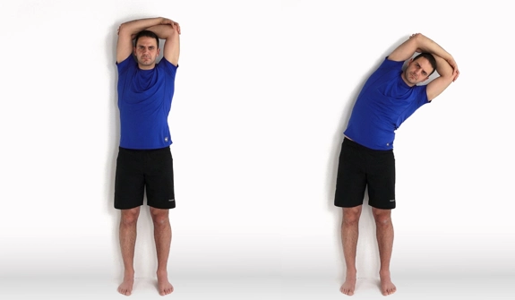 Person standing against a wall with arms crossed over their head, then leaning their upper body to the side.