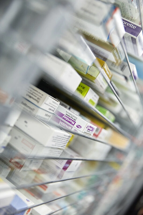 Closeup photo of medication boxes, stored on a glass shelf in a pharmacy