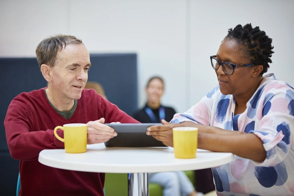 a Black staff member and a White staff member talking while looking at a tablet device