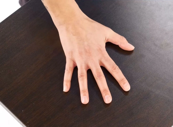 A hand flat palm-down on a table with fingers spread.