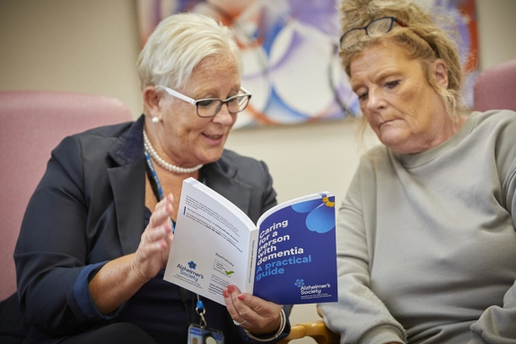 Staff Showing Booklet To patient called 'caring for a person with dementia - a practical guide'