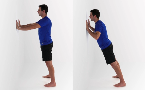 Person standing with hands on a wall, arms straight, and then leaning forward with elbows tucked into their sides.