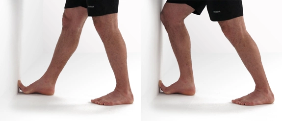 Person standing opposite a wall with toes on one foot against it, then bending the knee to increase the angle of the toes.