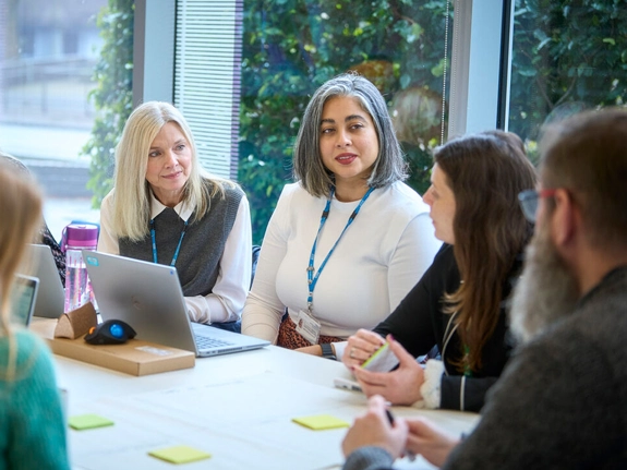 Group of staff at a meeting table with laptops and sticky notes