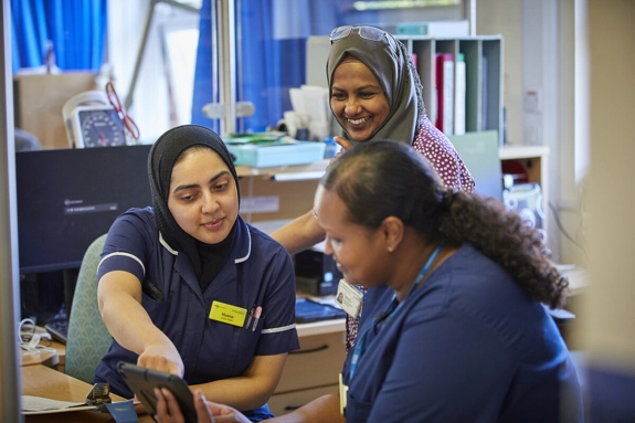 Three members of staff smiling and looking at tablet