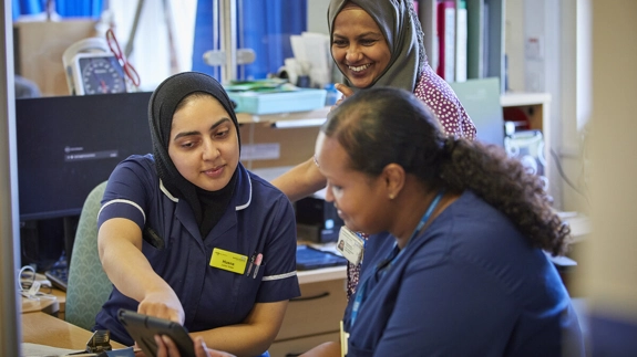 Three members of staff smiling and looking at tablet