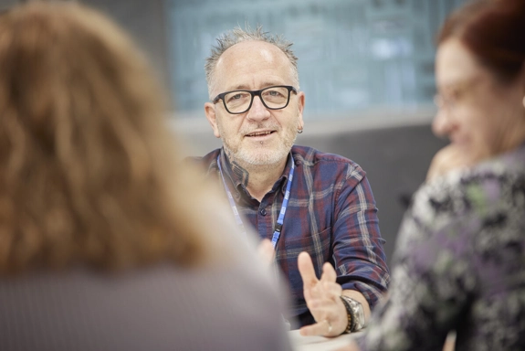 Staff member talking to two others, at a table