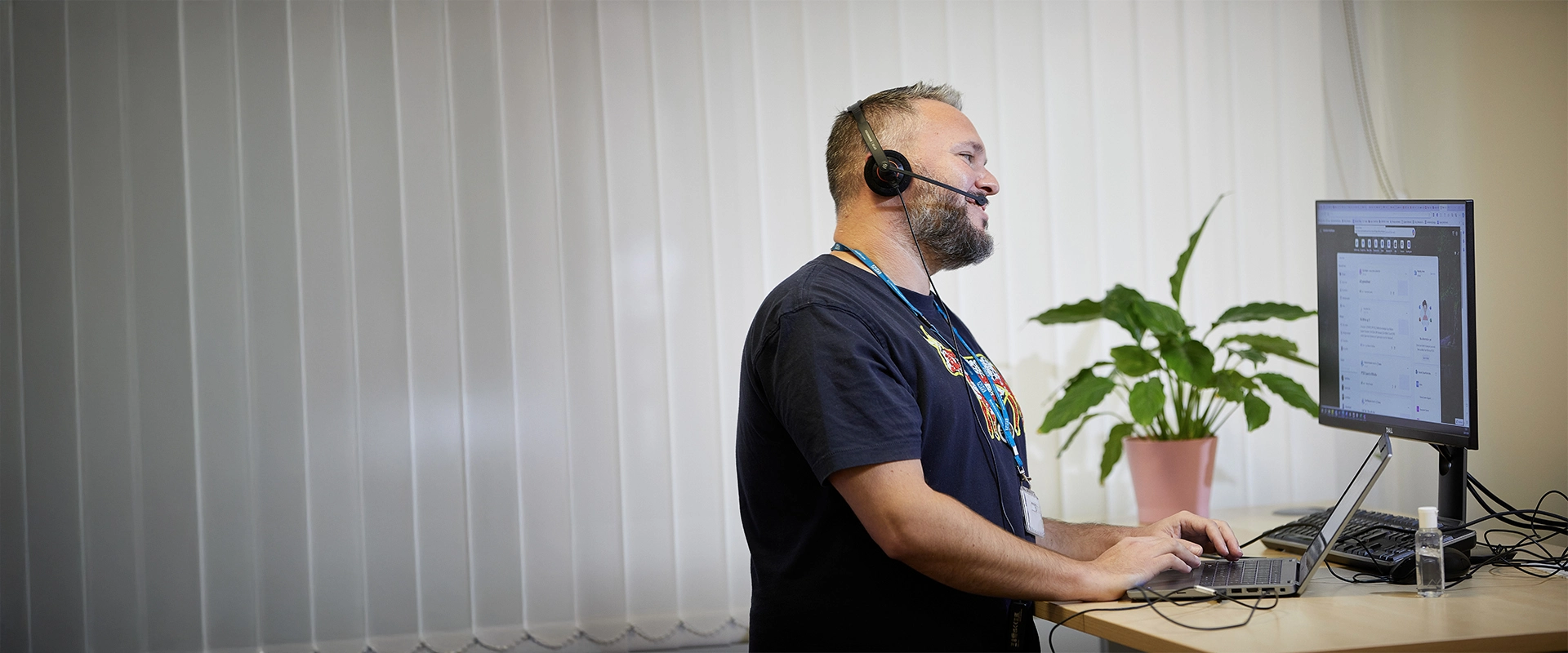 Staff member at a standing desk, using a laptop and talking using a headset
