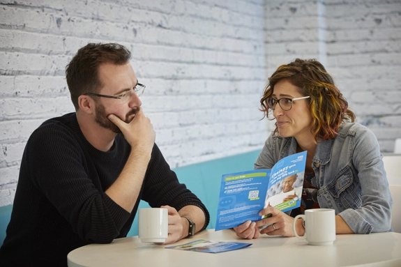 Two people discussing a leaflet while sitting at a table with a hot drink