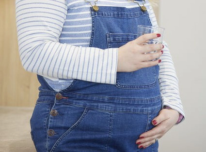 A closeup photo of a pregnant person, holding a glass of water