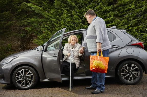 Carer helping older woman out of car