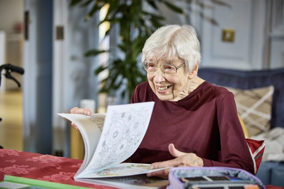 Older woman in a care home looking through the pages of a colouring book