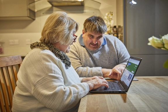 Carer sitting next to a woman at a table, looking at laptop