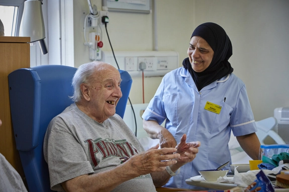 Nurse talking to a patient sitting in a ward chair after a meal