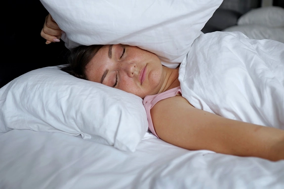 A closeup of a woman sleeping, while holding a pillow over the side of her head