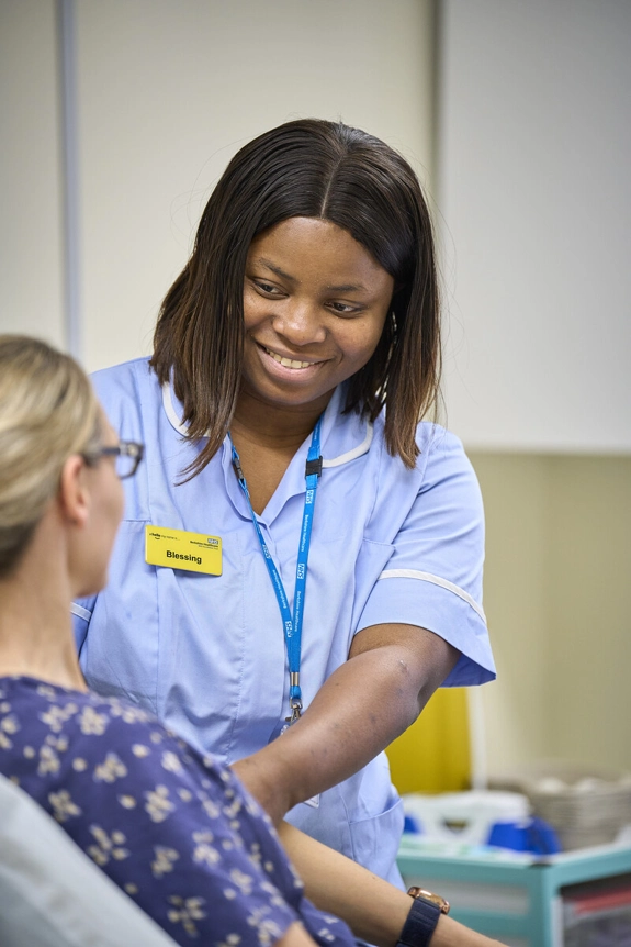 A Black ward nurse at St Marks, smiling at a patient sitting upright on a bed