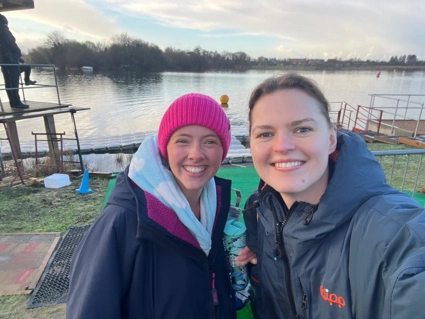 A selfie of two team members, smiling in front of lake